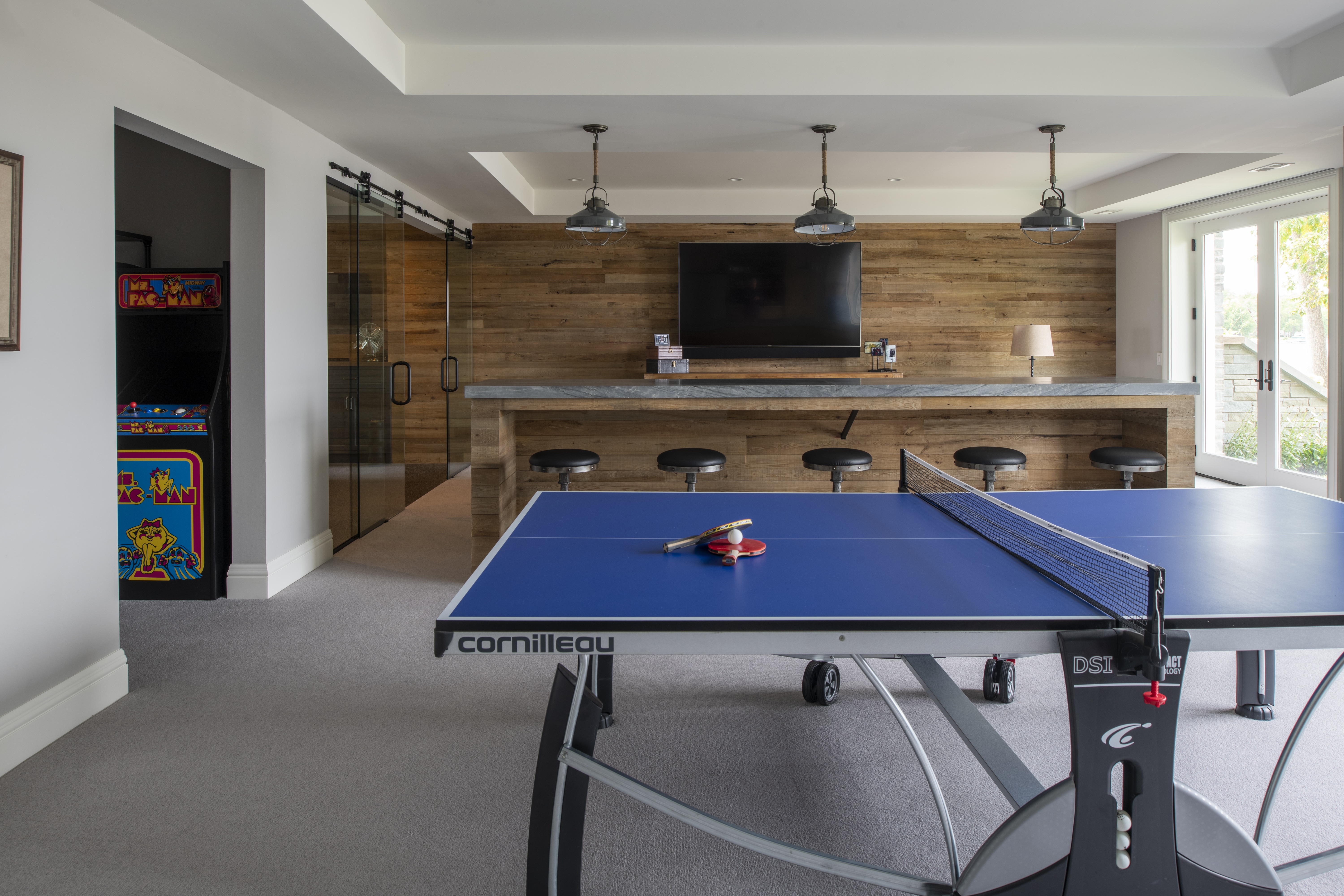 A rec room in a Gordon James custom luxury home features a ping pong table and mini bar.